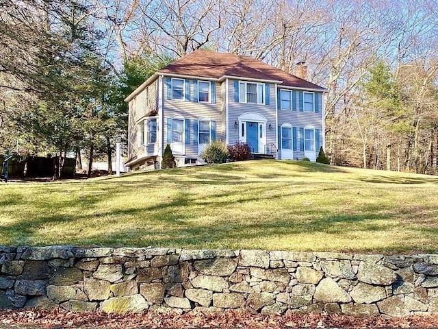 colonial inspired home featuring a chimney and a front lawn