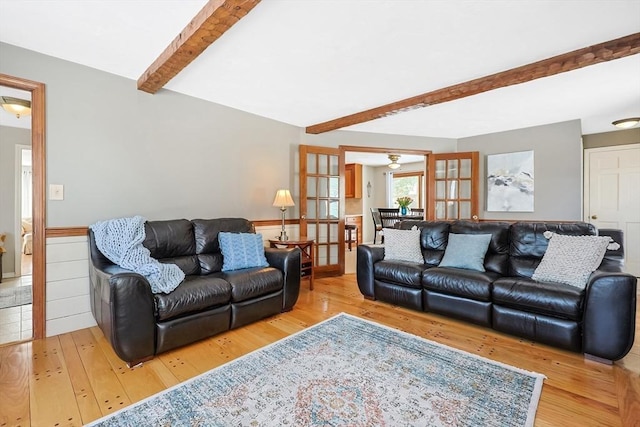 living area featuring a wainscoted wall, light wood finished floors, and beam ceiling