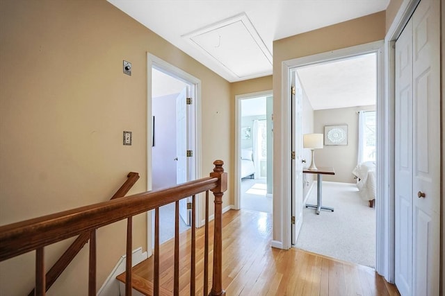 hall featuring light wood finished floors, attic access, baseboards, and an upstairs landing