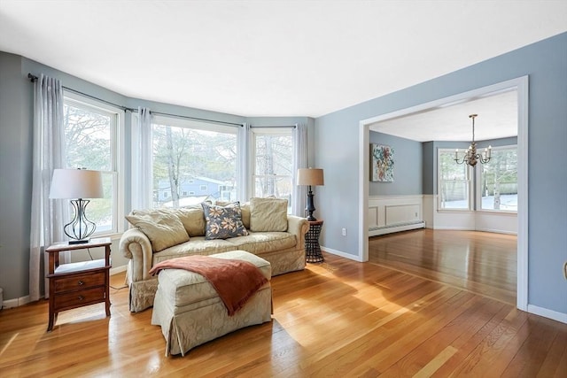 living area featuring a wealth of natural light, light wood-type flooring, a notable chandelier, and baseboard heating