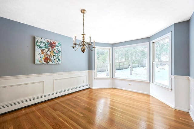 unfurnished dining area with a baseboard heating unit, a chandelier, wainscoting, and wood finished floors