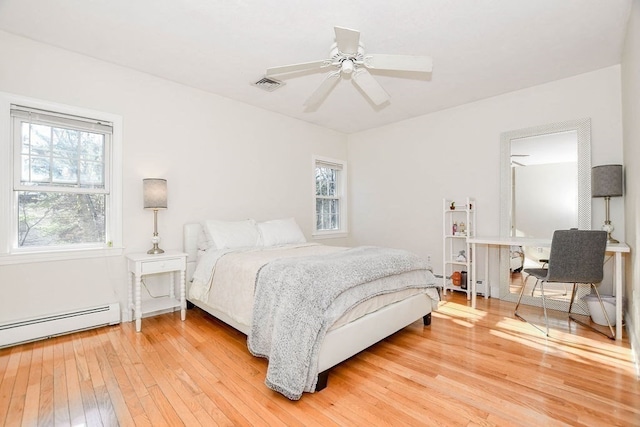 bedroom featuring hardwood / wood-style flooring, multiple windows, a baseboard heating unit, and ceiling fan