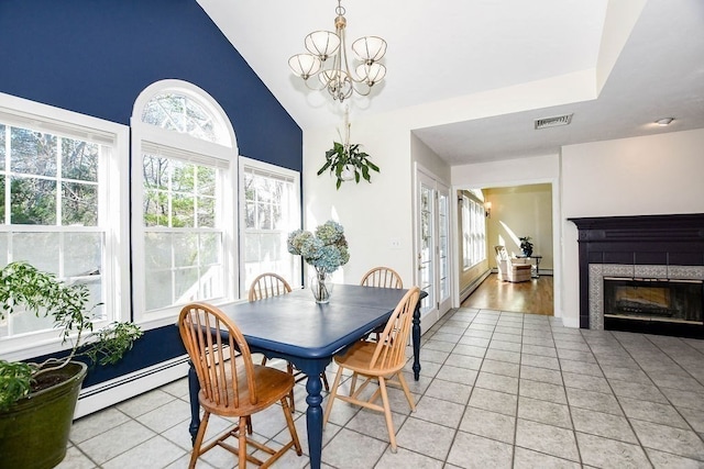 tiled dining space featuring a tile fireplace, lofted ceiling, an inviting chandelier, and a baseboard heating unit