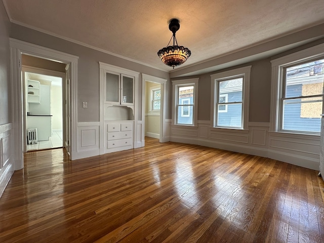 interior space with ornamental molding, a textured ceiling, wood-type flooring, and radiator heating unit