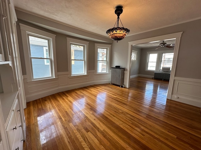 unfurnished dining area with ceiling fan, ornamental molding, radiator heating unit, and hardwood / wood-style floors