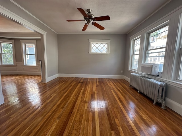 empty room with a wealth of natural light, ornamental molding, dark wood-type flooring, and radiator heating unit