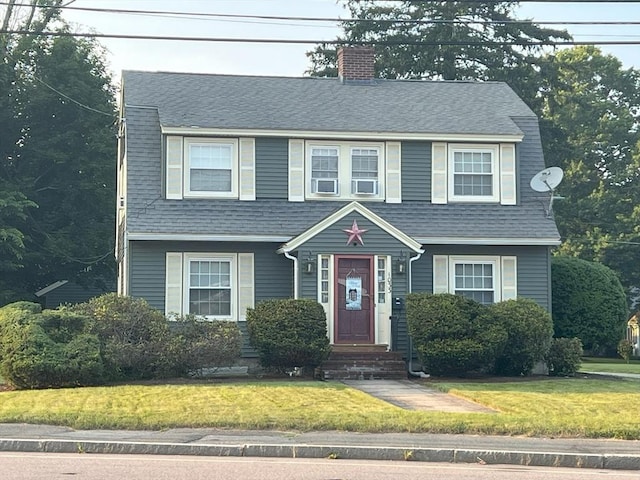 view of front facade with a front yard, a chimney, and a shingled roof