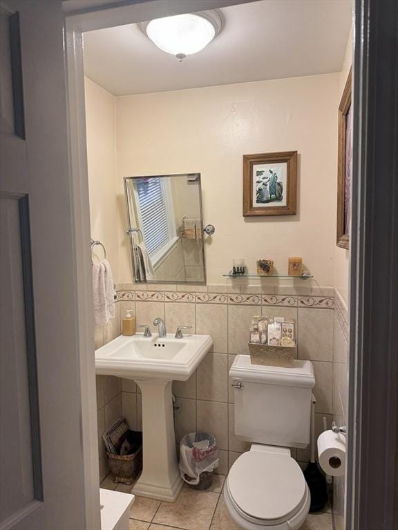 bathroom with a wainscoted wall, toilet, a sink, tile walls, and tile patterned floors