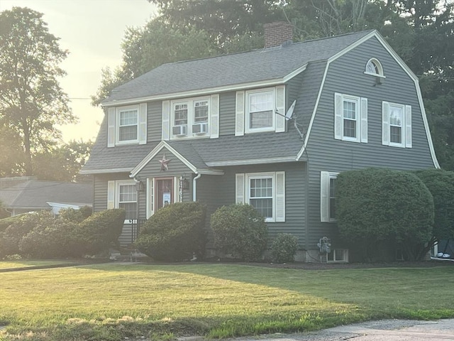 colonial inspired home with a front yard, roof with shingles, a gambrel roof, and a chimney