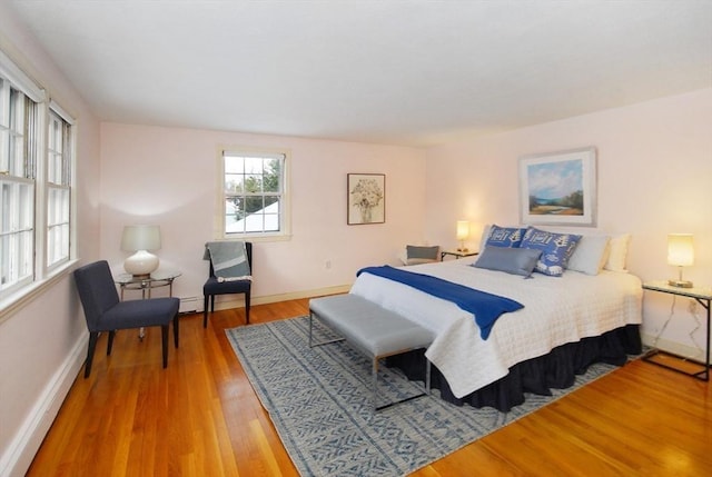 bedroom with light wood-type flooring, a baseboard heating unit, and baseboards