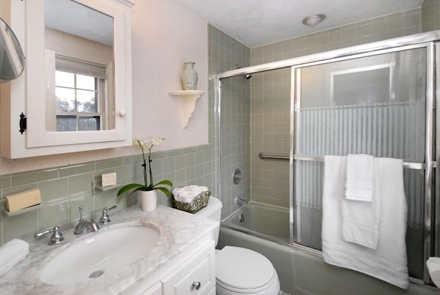 bathroom with toilet, enclosed tub / shower combo, tile walls, and vanity