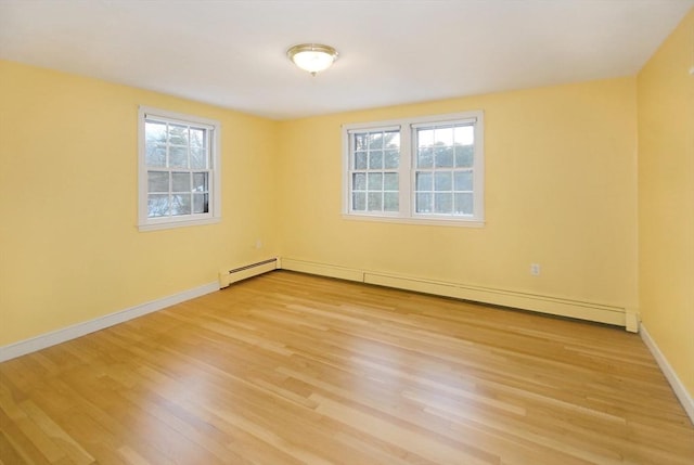 empty room with a baseboard heating unit, a wealth of natural light, light wood-style floors, and baseboards