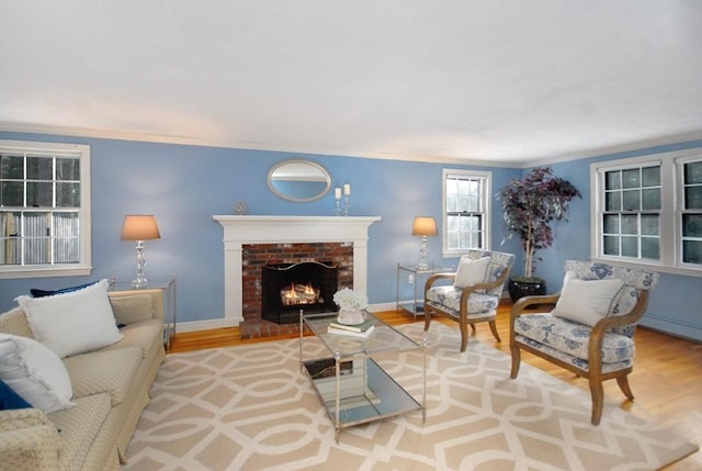 living area with a brick fireplace, crown molding, baseboards, and wood finished floors