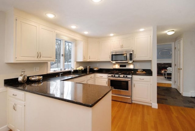 kitchen with a peninsula, light wood-type flooring, appliances with stainless steel finishes, and white cabinets