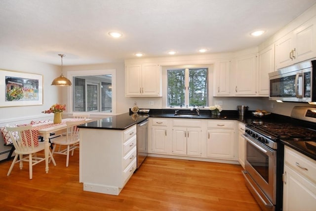 kitchen with light wood finished floors, stainless steel appliances, dark countertops, white cabinets, and a peninsula