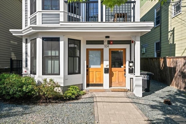 view of exterior entry with a balcony, fence, and a porch