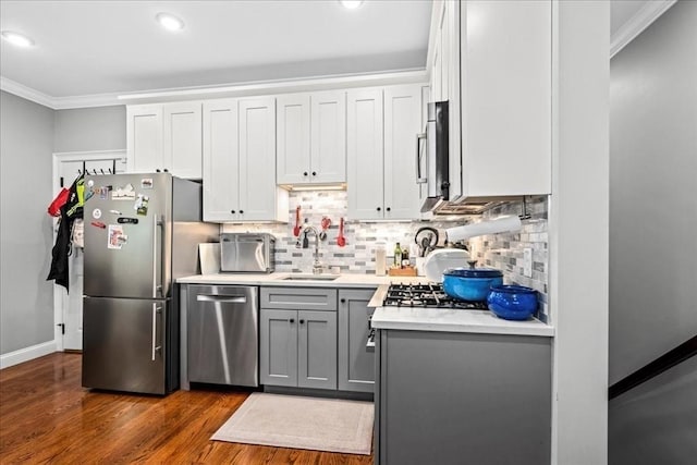 kitchen featuring appliances with stainless steel finishes, a sink, ornamental molding, gray cabinets, and light countertops
