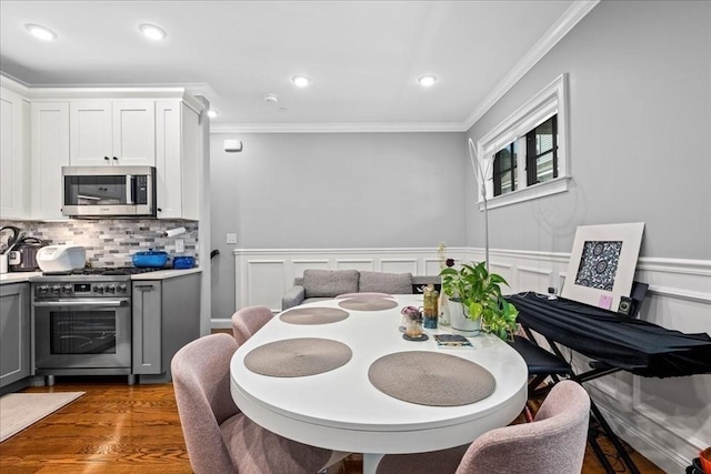 dining space featuring crown molding, dark wood-type flooring, recessed lighting, and wainscoting