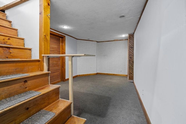 basement featuring carpet floors, ornamental molding, a textured ceiling, and brick wall