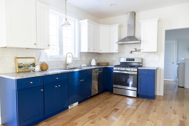 kitchen with wall chimney range hood, blue cabinets, a sink, and appliances with stainless steel finishes