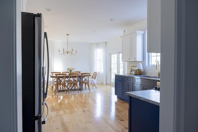 kitchen featuring light wood-style flooring, white cabinetry, freestanding refrigerator, decorative backsplash, and a sink