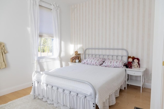 bedroom featuring wood finished floors, baseboards, and wallpapered walls