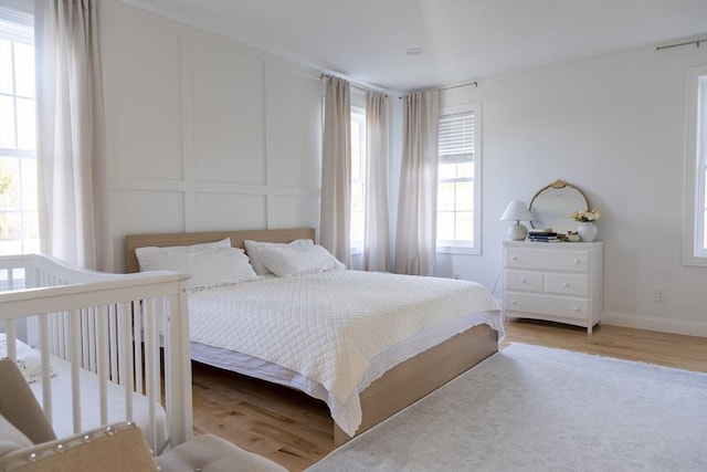 bedroom with a decorative wall, baseboards, and light wood finished floors
