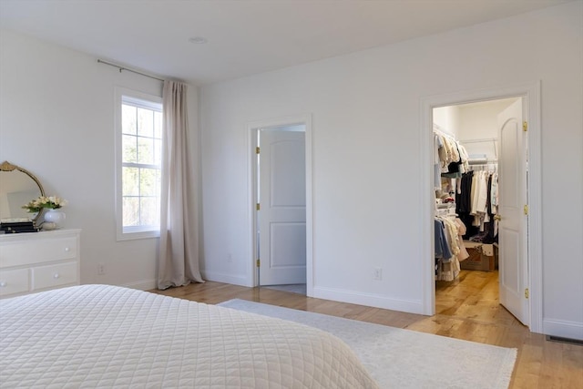 bedroom featuring a closet, a spacious closet, light wood-style floors, and baseboards