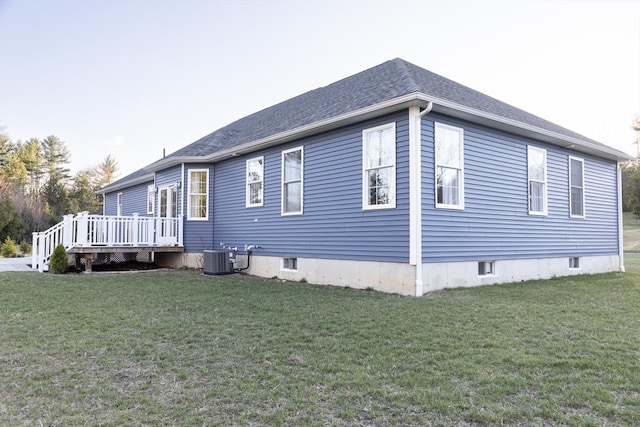 view of home's exterior featuring central air condition unit, a shingled roof, a wooden deck, and a lawn