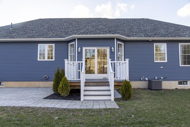 rear view of house featuring a patio area, a shingled roof, central AC, and a lawn