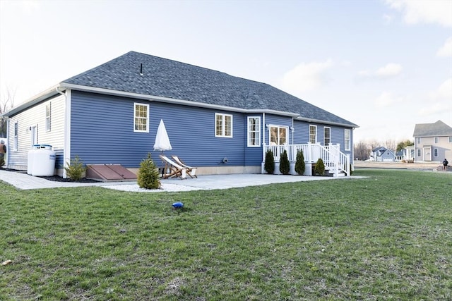 back of property featuring a patio area, a shingled roof, and a lawn