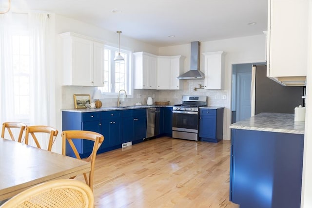 kitchen featuring wall chimney exhaust hood, tasteful backsplash, blue cabinetry, white cabinetry, and appliances with stainless steel finishes