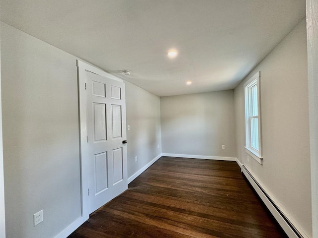 spare room featuring a baseboard heating unit and dark hardwood / wood-style floors