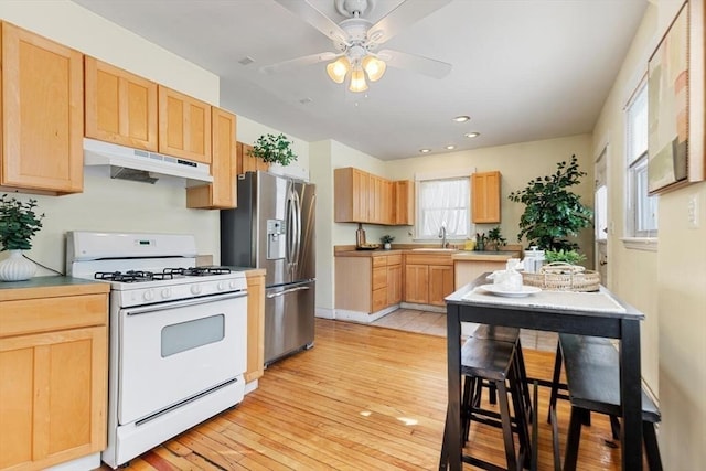 kitchen with under cabinet range hood, a sink, stainless steel refrigerator with ice dispenser, light brown cabinetry, and gas range gas stove