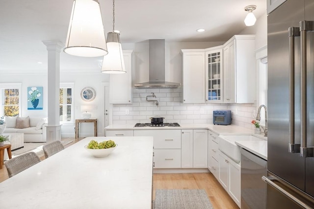 kitchen with wall chimney range hood, glass insert cabinets, stainless steel appliances, and decorative backsplash