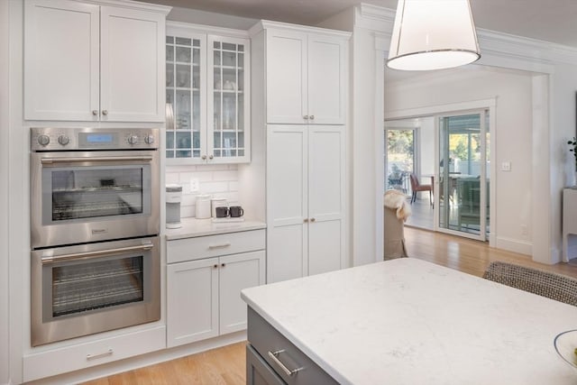 kitchen featuring decorative backsplash, ornamental molding, stainless steel double oven, glass insert cabinets, and light wood-style floors