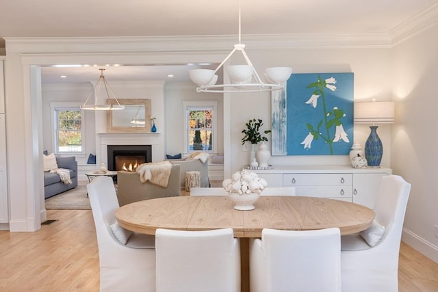 dining room featuring light wood-type flooring, a warm lit fireplace, baseboards, and crown molding