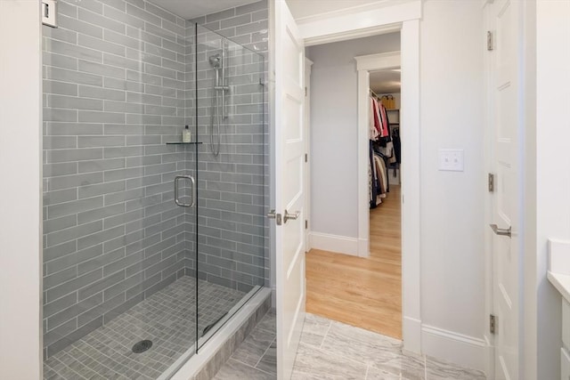 full bathroom featuring a stall shower, baseboards, a walk in closet, and wood finished floors