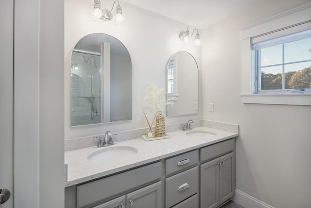 bathroom featuring double vanity, a shower with door, baseboards, and a sink