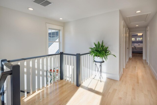 hallway with a wealth of natural light, light wood-type flooring, visible vents, and baseboards