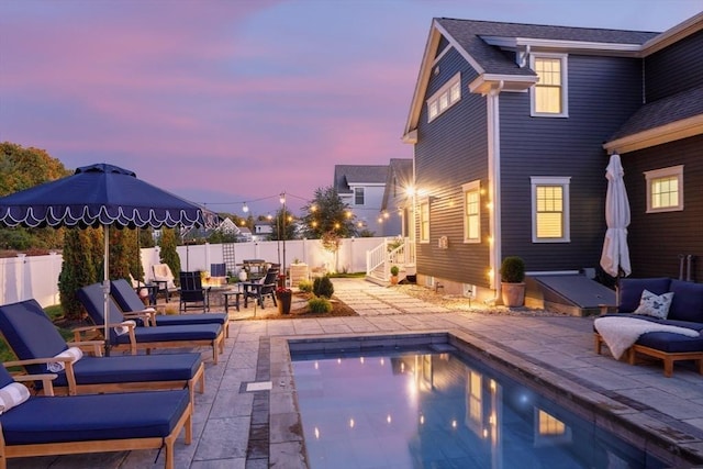 pool at dusk with a patio area, a fenced backyard, an outdoor living space, and a fenced in pool