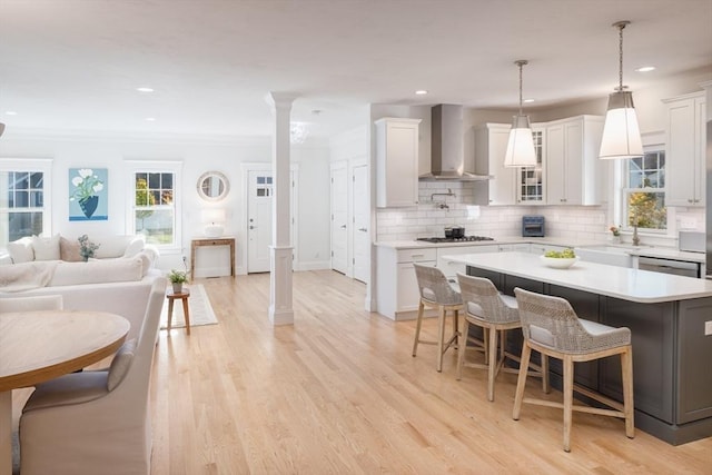 kitchen featuring light countertops, backsplash, appliances with stainless steel finishes, wall chimney range hood, and ornate columns