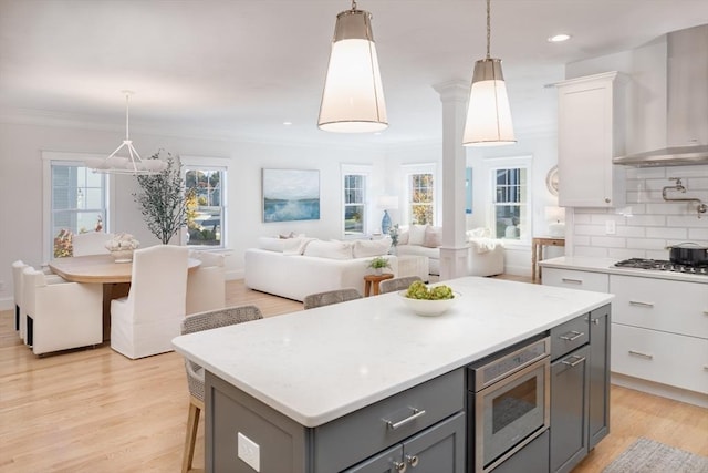 kitchen featuring tasteful backsplash, wall chimney exhaust hood, appliances with stainless steel finishes, light countertops, and gray cabinetry