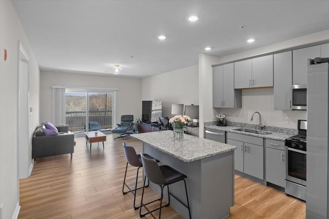 kitchen featuring gray cabinets, a sink, appliances with stainless steel finishes, a kitchen bar, and open floor plan