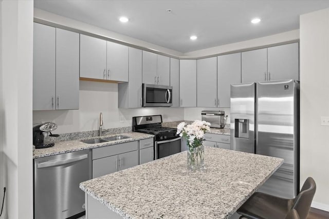 kitchen featuring a kitchen island, a breakfast bar, light stone counters, appliances with stainless steel finishes, and a sink