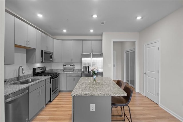 kitchen with a kitchen island, gray cabinets, a sink, stainless steel appliances, and a kitchen breakfast bar