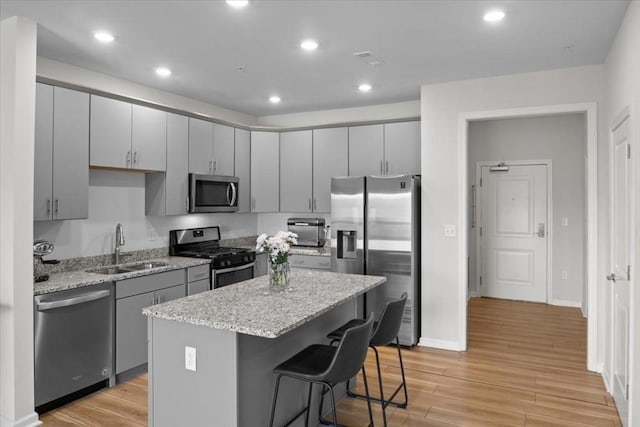 kitchen featuring gray cabinets, a sink, a kitchen island, light wood-style floors, and appliances with stainless steel finishes