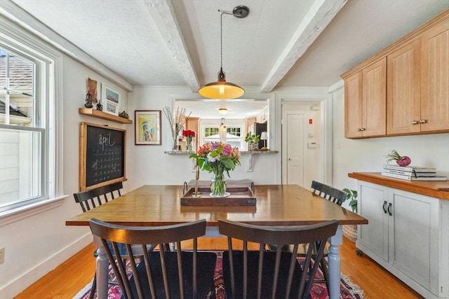 dining room with baseboards, light wood-style flooring, and beam ceiling