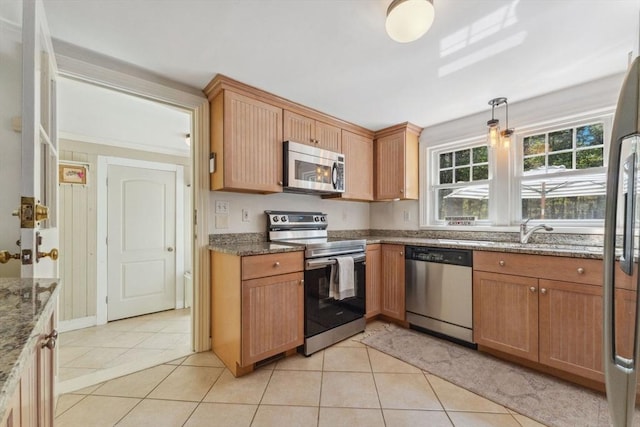 kitchen featuring light tile patterned flooring, appliances with stainless steel finishes, a sink, dark stone countertops, and pendant lighting