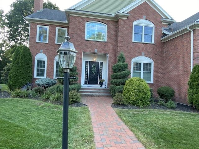 view of front of property featuring a front yard, brick siding, and a chimney